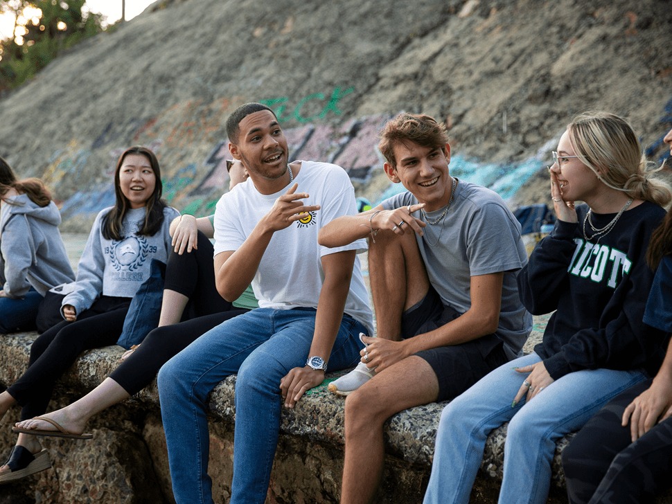 A diverse group of college students sit together outdoors, smiling and chatting.