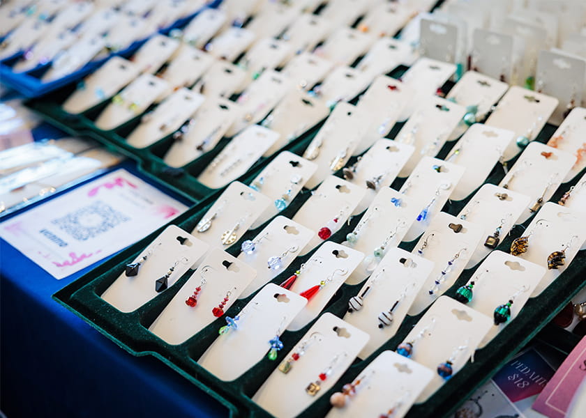 Rows of handmade dangling earrings on white card backing arranged neatly in display trays at a pop-up shop.