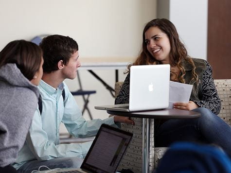 two girls and a guy studying and talking with each other with their laptops