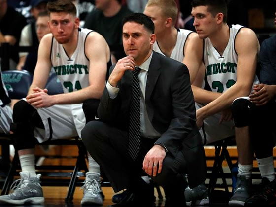 the gulls basketball coach squatting in front of his bench