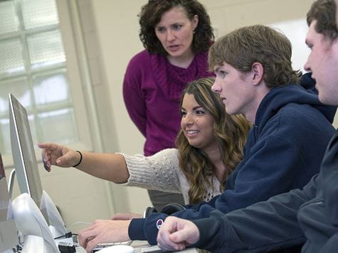 a girl pointing to her classmate's screen with a professor looking over