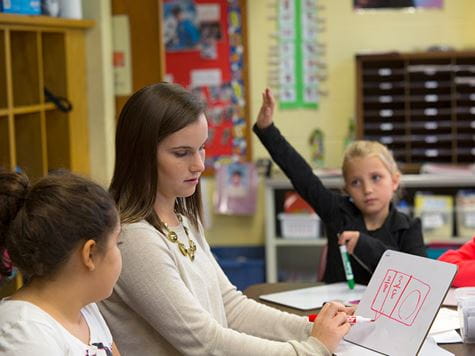 a kid raising her hand for the education student instructing a class