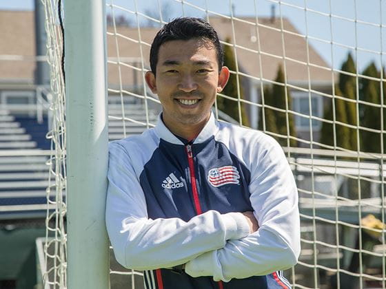 a soccer coach in a jacket leaning on a goalpost