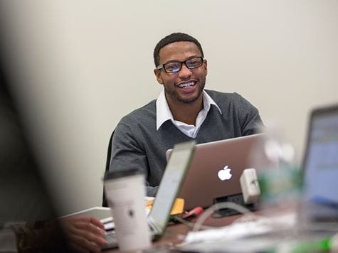 a man smiling in front of his laptop