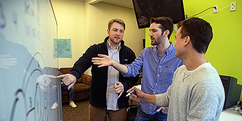 Three computer science students working together at a white board