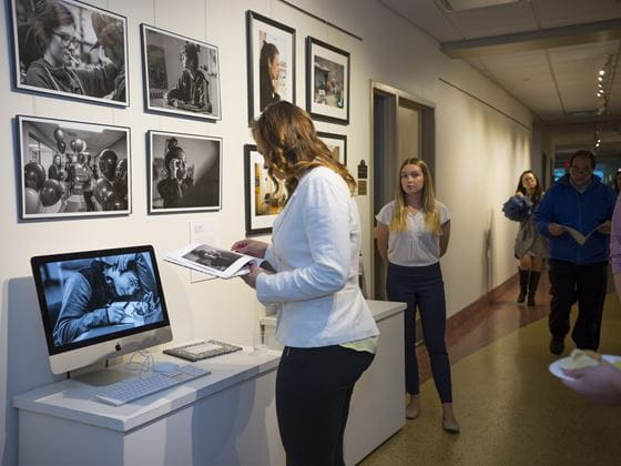 a woman looking at a book in front of a computer in a hall with other students