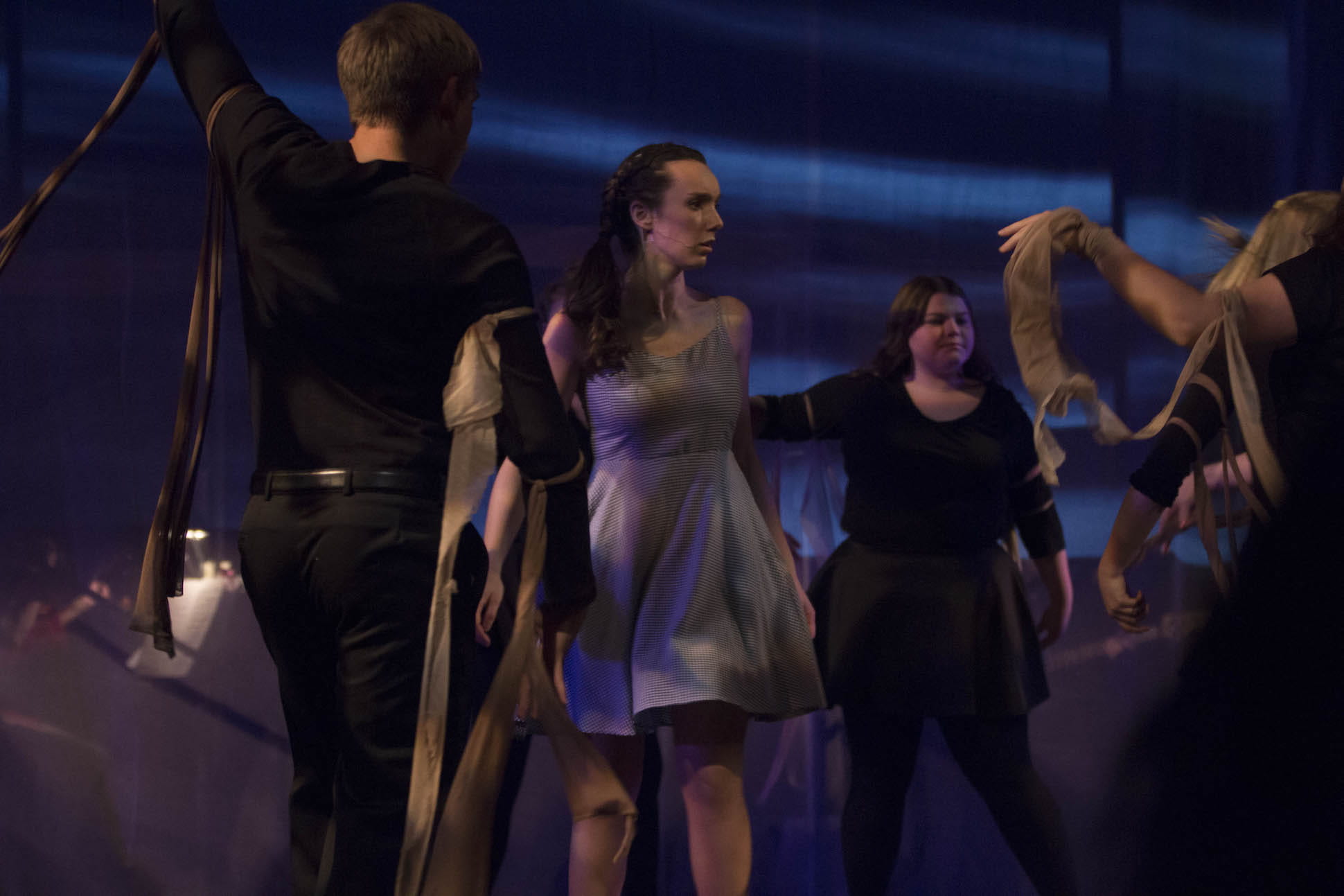 actors dance and sing in dark setting of stage