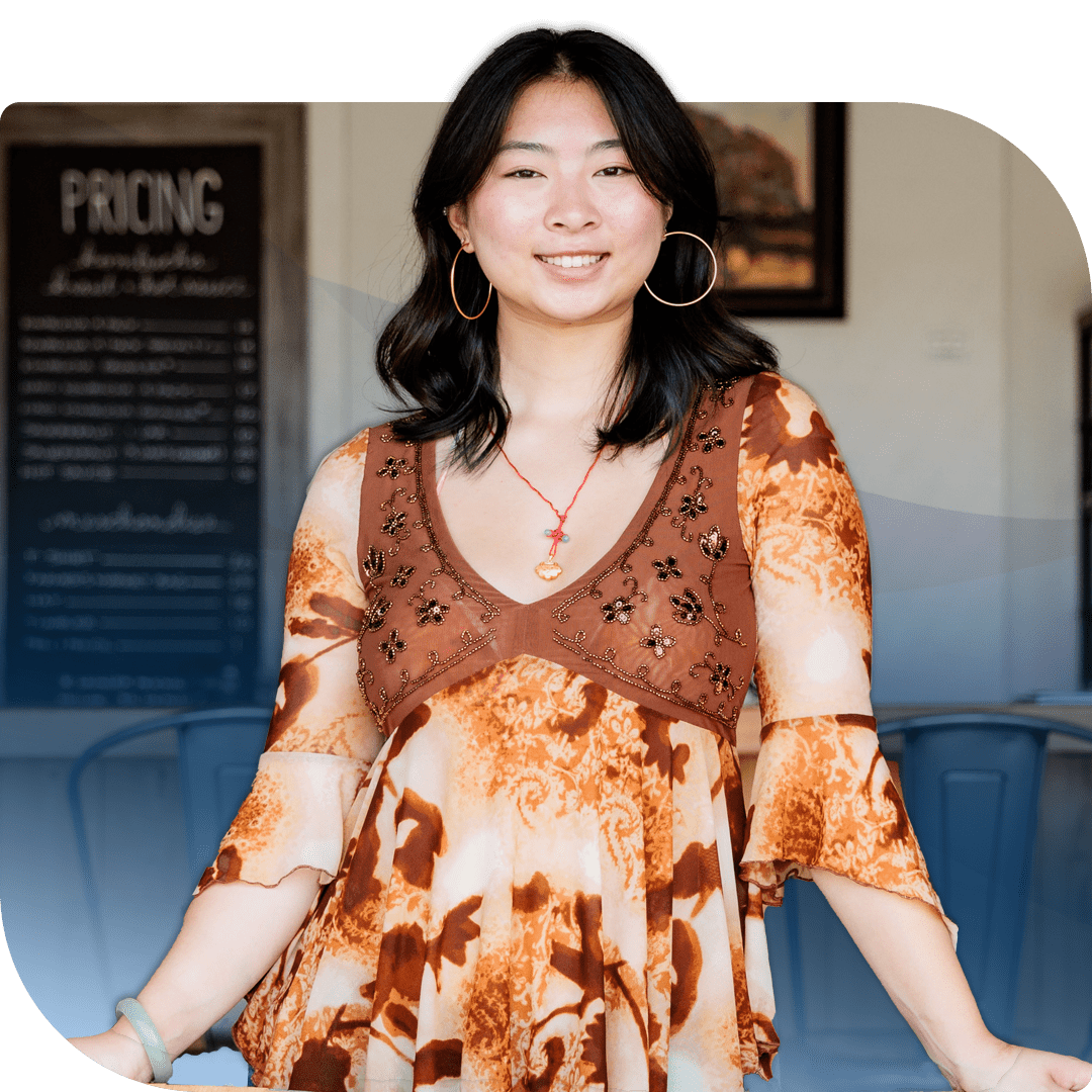 A young woman with dark hair and large hoop earrings smiles in front of a menu board.