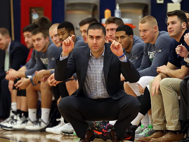 a coach squatting and signalling with his fingers on the sideline
