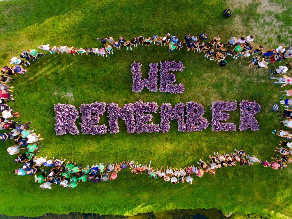 a top-down view of many people standing around the words 'we remember' spelled out with US flags