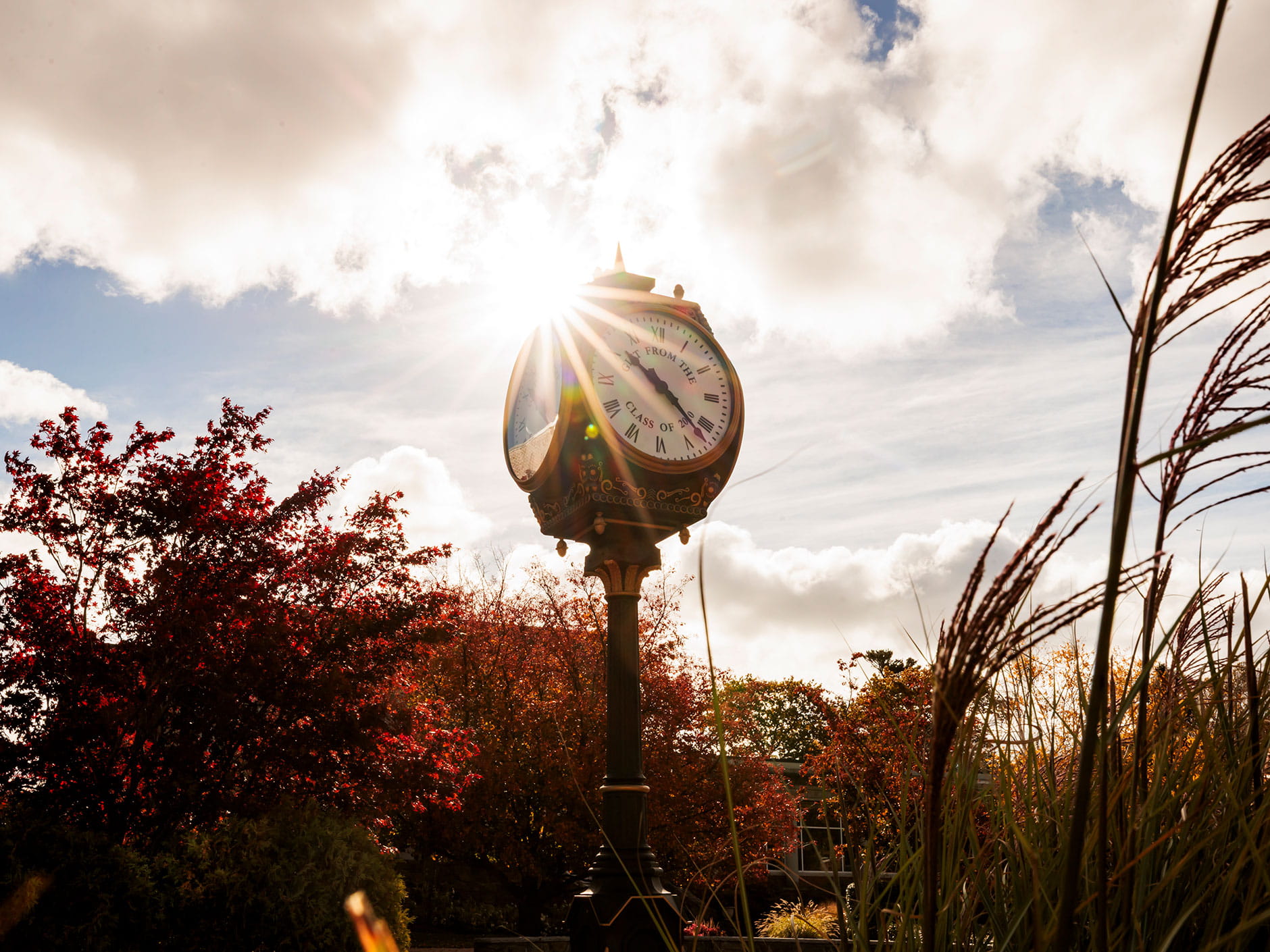Sun peaks through the fall skies and shines on a clocktower on Endicott College's campus