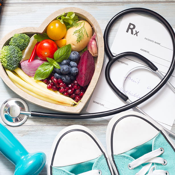 Fruit in a heart-shaped bowl with a stethoscope, running shoes and a dumbbell