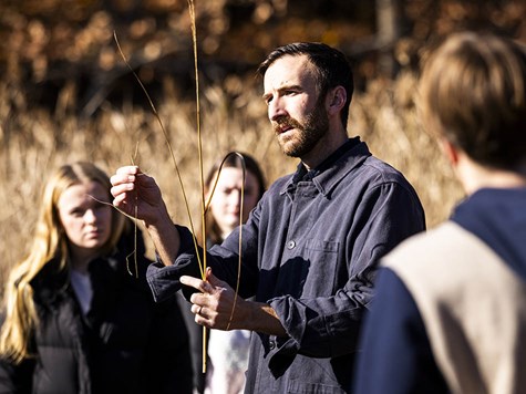 An instructor holding up dried plant stalks outdoor while teaching a group of students.