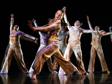 A group of dancers wearing matching earth-toned outfits performing a expressive routine on stage.
